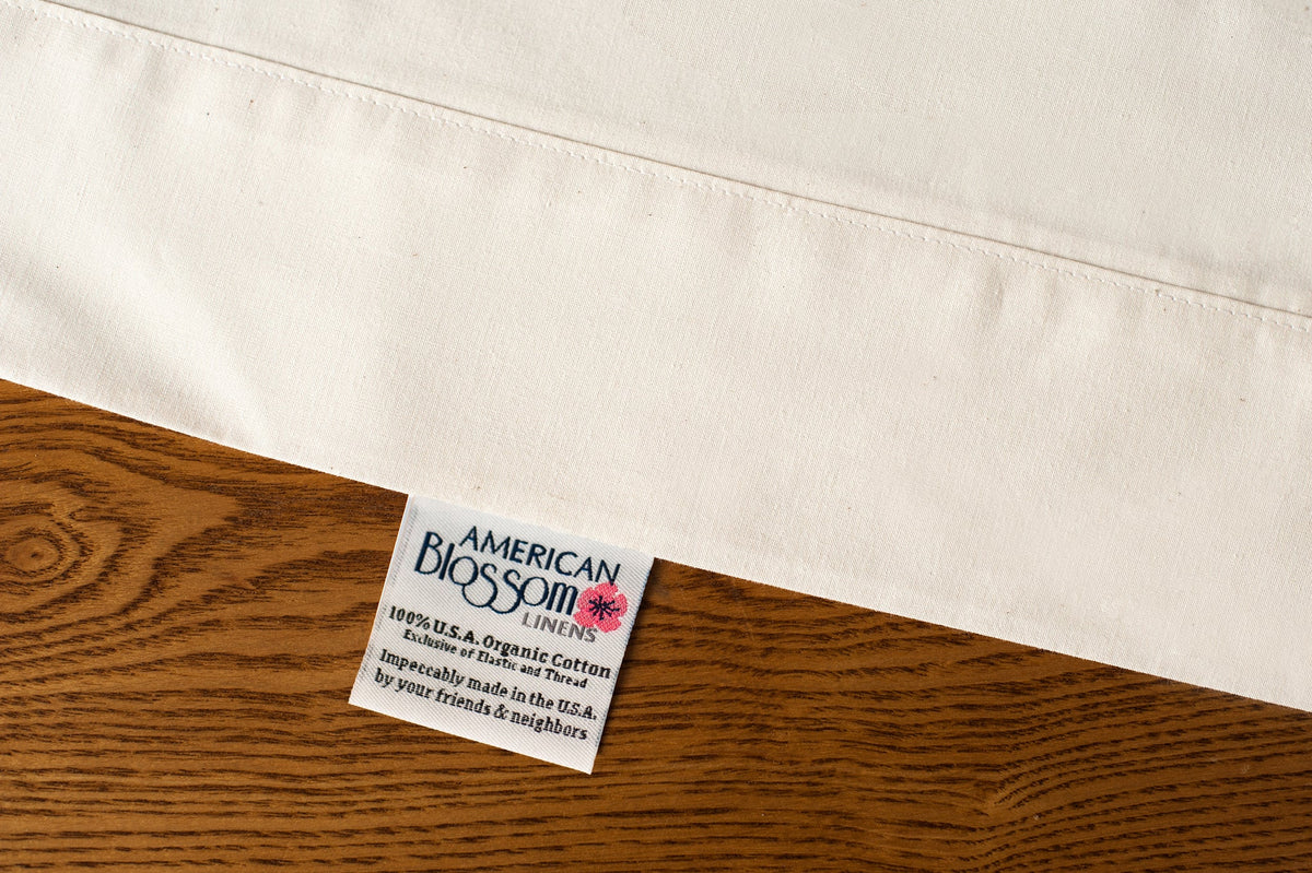 Flat organic cotton sheet in natural color displaying american blossom linens tag.