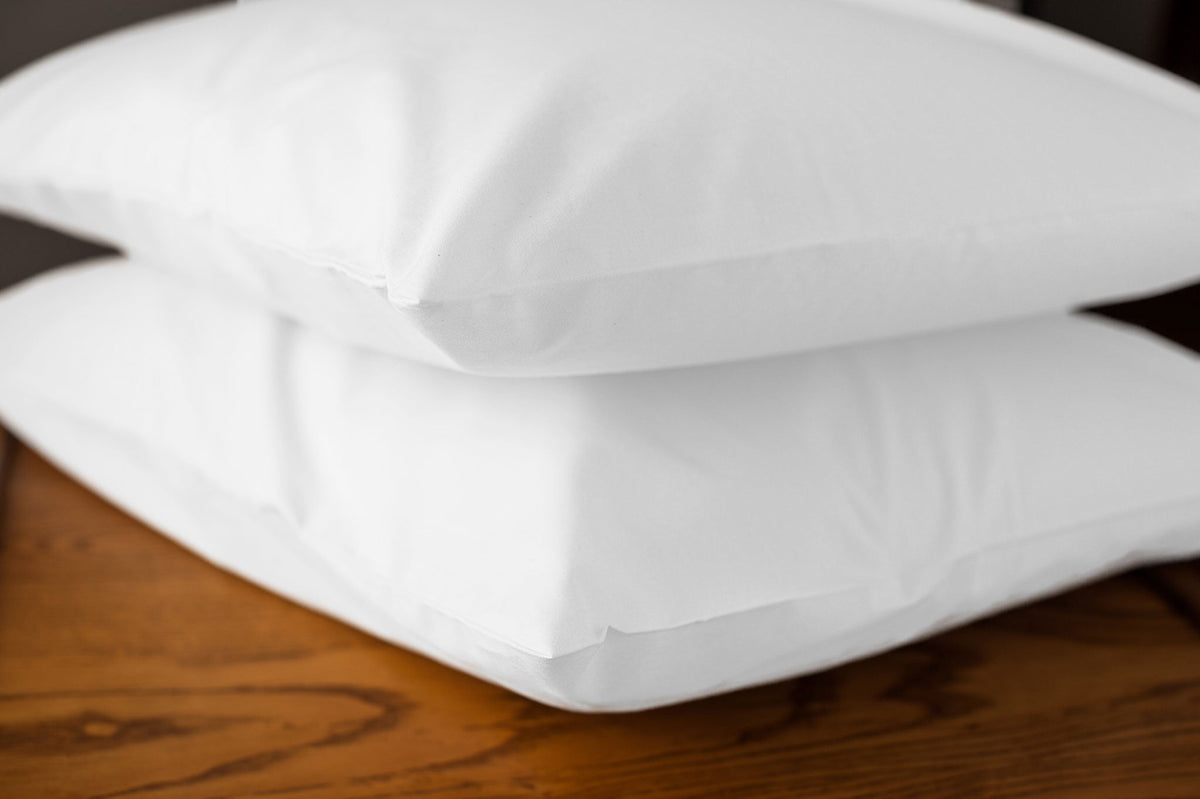 White organic cotton pillowcases with pillows stacked on a nightstand.