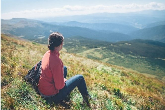 Woman Sitting on the side of a hill looking over a valley and mountains.