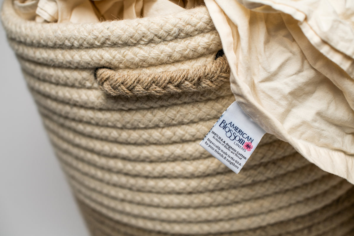 Close up of two tone beige American made natural wool hamper with American Blossom Linens natural sheets in it. 