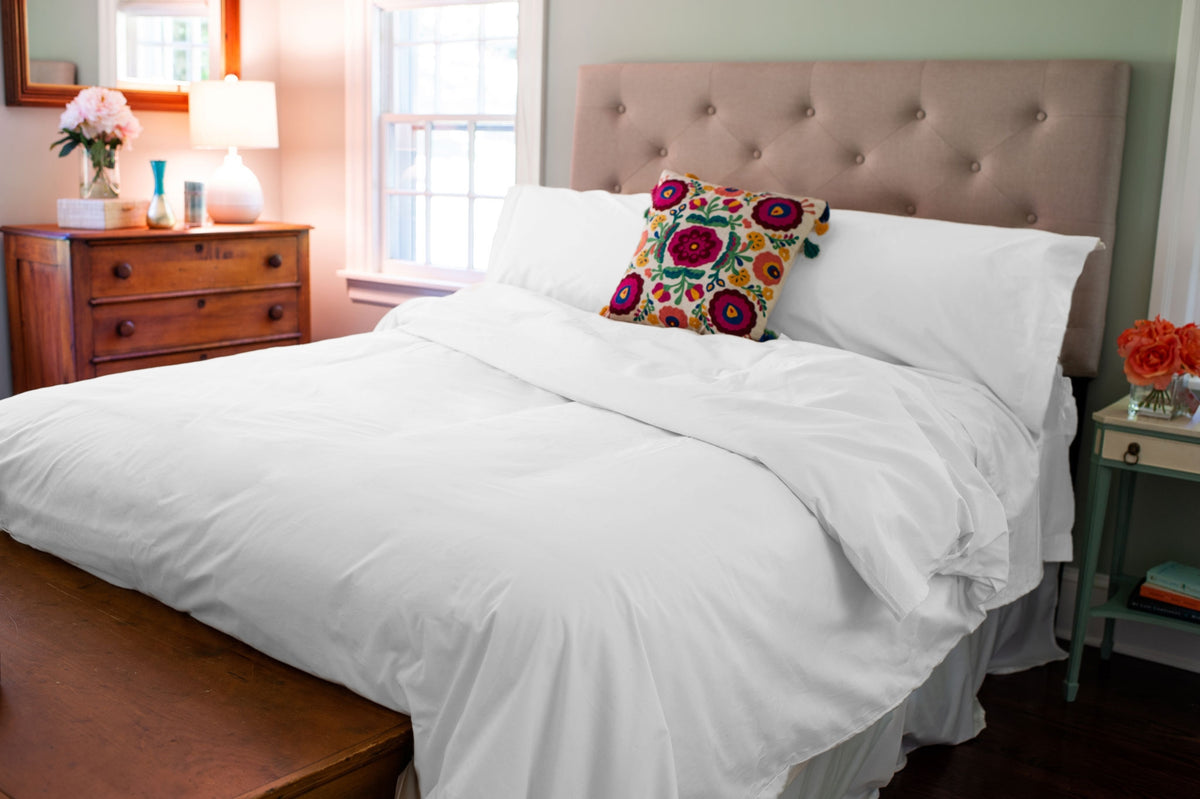 White organic cotton duvet cover set and pillow shams on a freshly made bed in a bedroom.