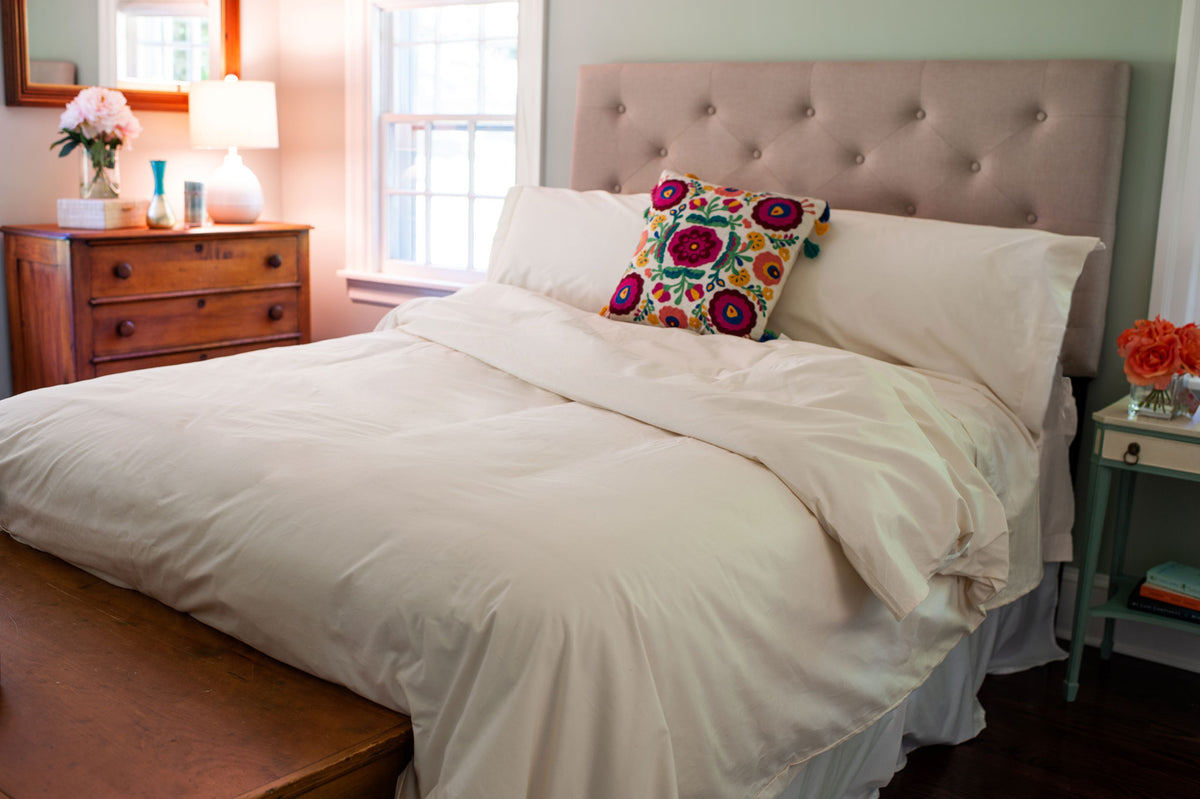 Organic cotton duvet cover set and pillow shams in natural color on a freshly made bed in a bedroom.