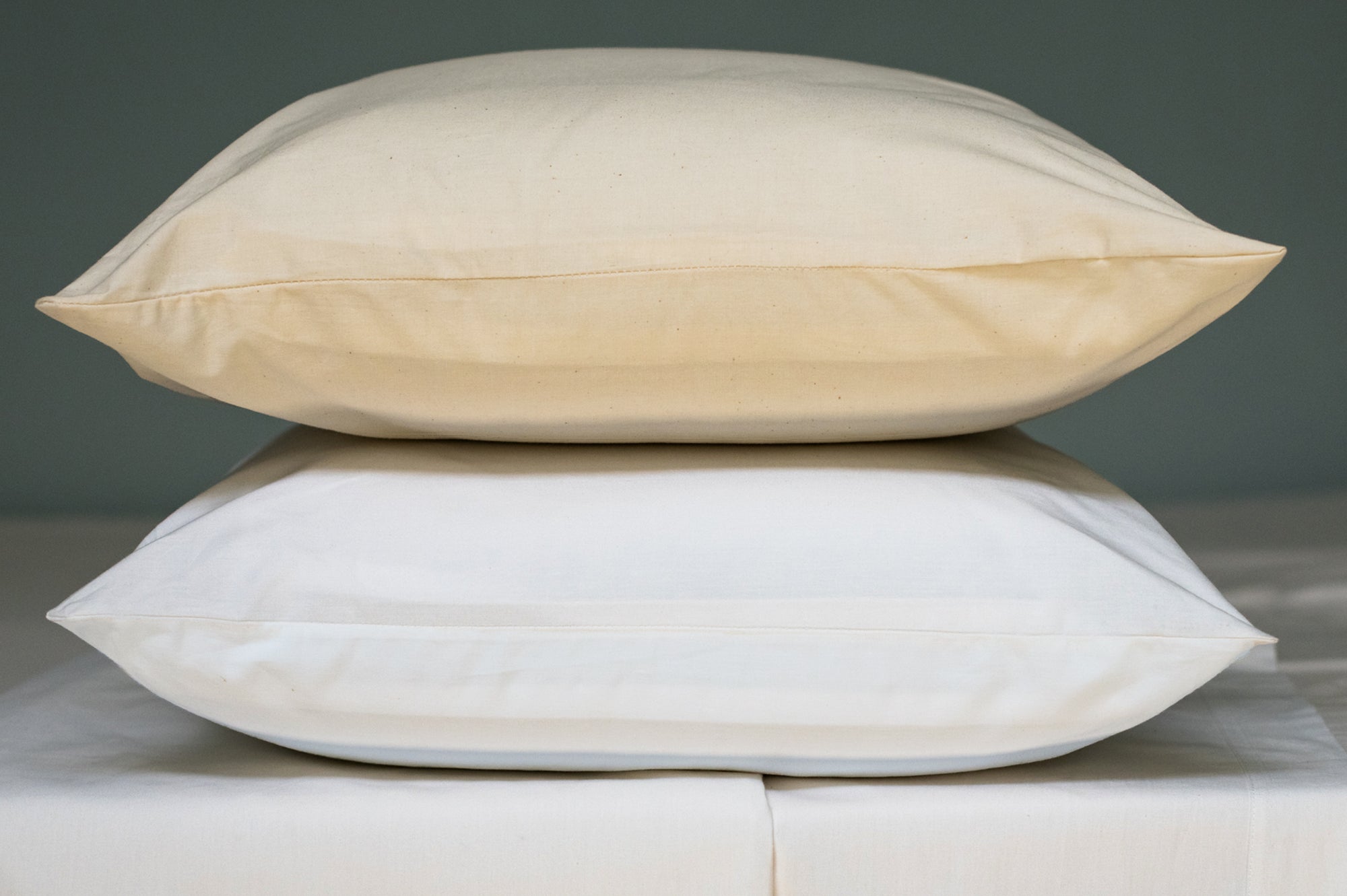 Organic cotton pillowcases in natural and white color with pillows stacked on a bed.