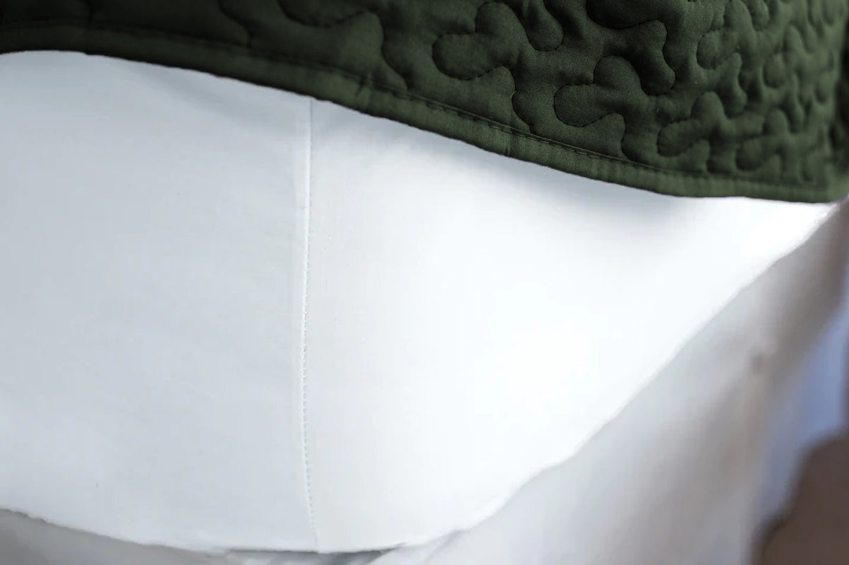 Corner of mattress made with white organic cotton fitted sheet with a green bedspread.